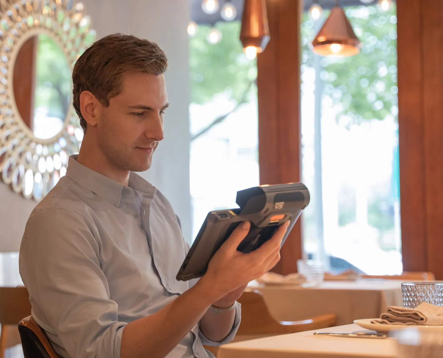 Serveur consultant un terminal mobile AltosPOS en salle de restaurant
